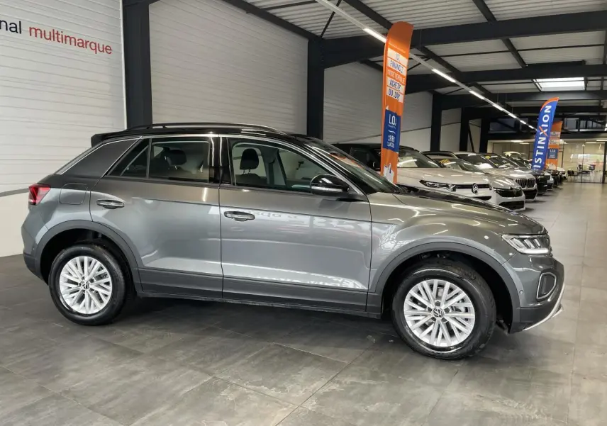 Volkswagen T-Roc 2025 gris Indium, vue de profil côté gauche en intérieur avec toit noir et jantes alliage.