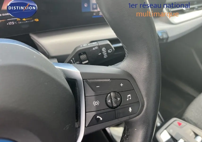 Gros plan sur la partie droite du volant noir d’une BMW Série 2 Active Tourer 225e xDrive grise, avec commandes multimédia visibles.