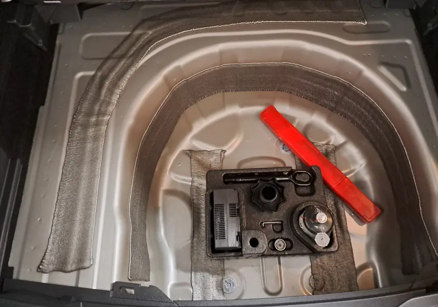 Coffre ouvert du Volkswagen Taigo 2024, vue plongeante sur l'emplacement de la roue de secours avec outils et triangle de signalisation rouge.
