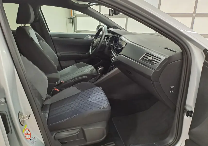 Intérieur avant du Volkswagen Taigo 2024 en Reflet d'argent, sièges tissu noir à motifs, tableau de bord moderne côté passager.