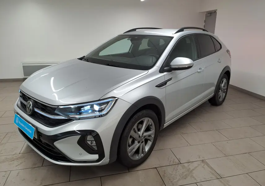 Volkswagen Taigo 1.0 TSI R-Line 2024 en reflet d'argent, vue 3/4 avant droit avec phares allumés et jantes alliage.