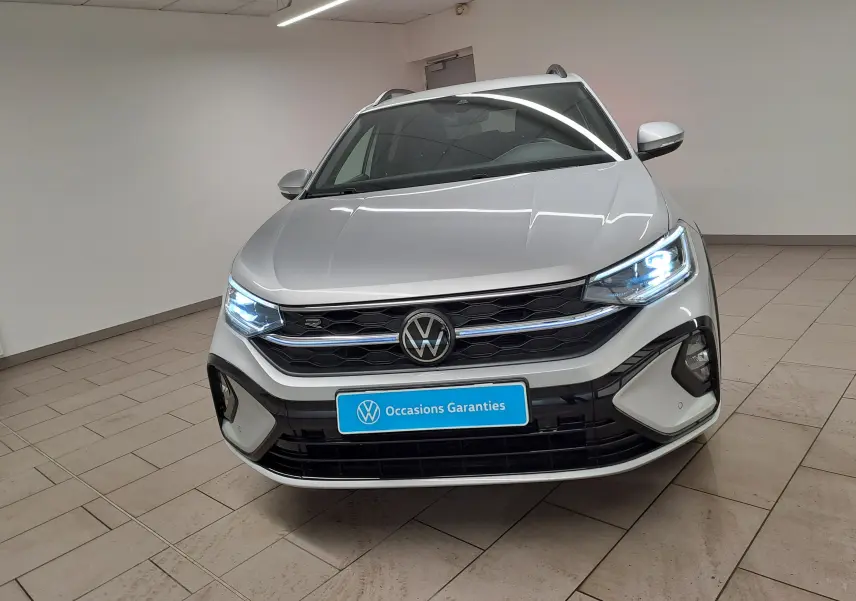Volkswagen Taigo 2024 R-Line en reflet d'argent, vue avant avec phares allumés dans un intérieur showroom.