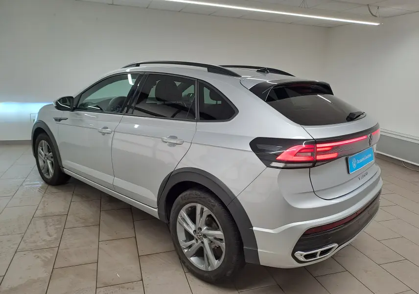 Volkswagen Taigo 2024 R-Line en reflet d'argent, vue 3/4 arrière droit avec feux arrière allumés en intérieur.
