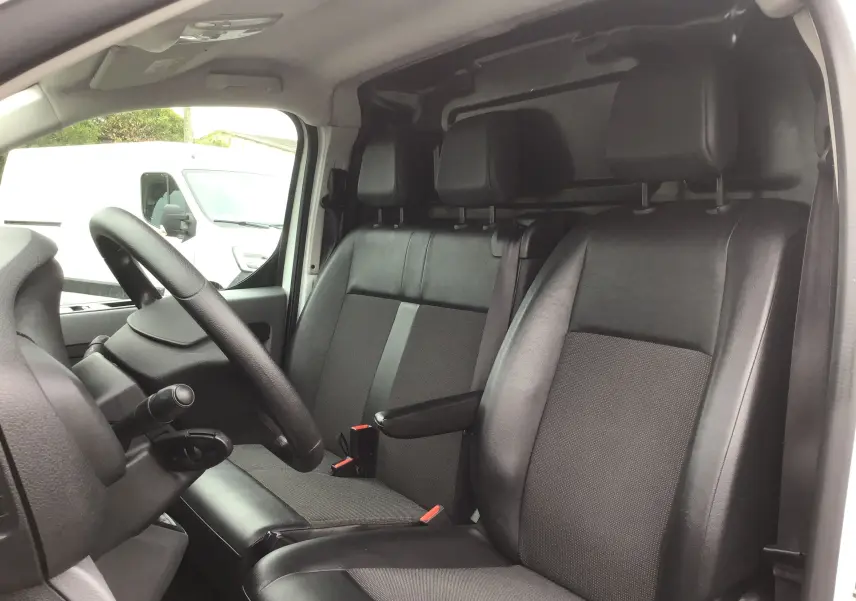 Vue intérieure côté conducteur de l'Opel Vivaro blanc 2022, sièges noirs en cuir et tissu avec accoudoir central.