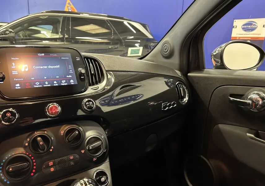 Intérieur côté passager de la Fiat 500 noire 2023, tableau de bord brillant avec logo 500 et écran tactile allumé.