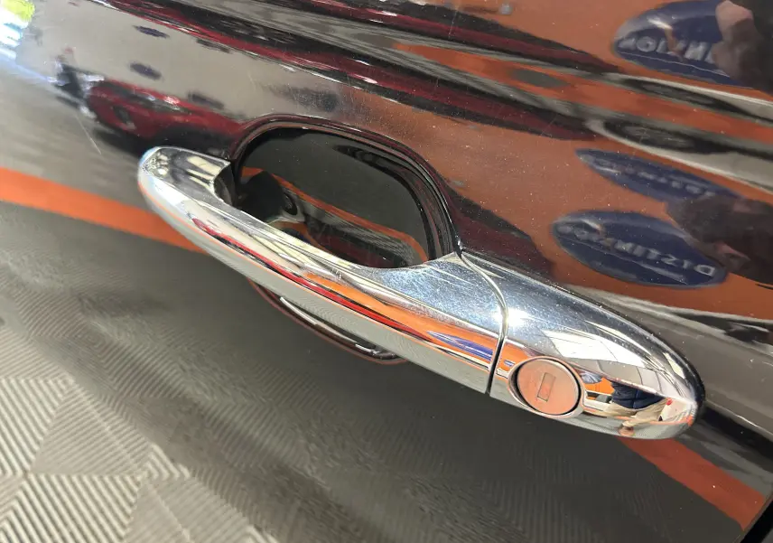 Poignée de porte chromée en gros plan sur la portière noire d'une FIAT 500 2023 avec radar de recul.