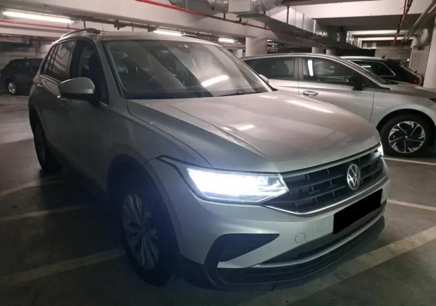 Volkswagen Tiguan 2.0 TDI 2022 en argent fleuret, vue 3/4 avant avec phares LED allumés dans un parking.