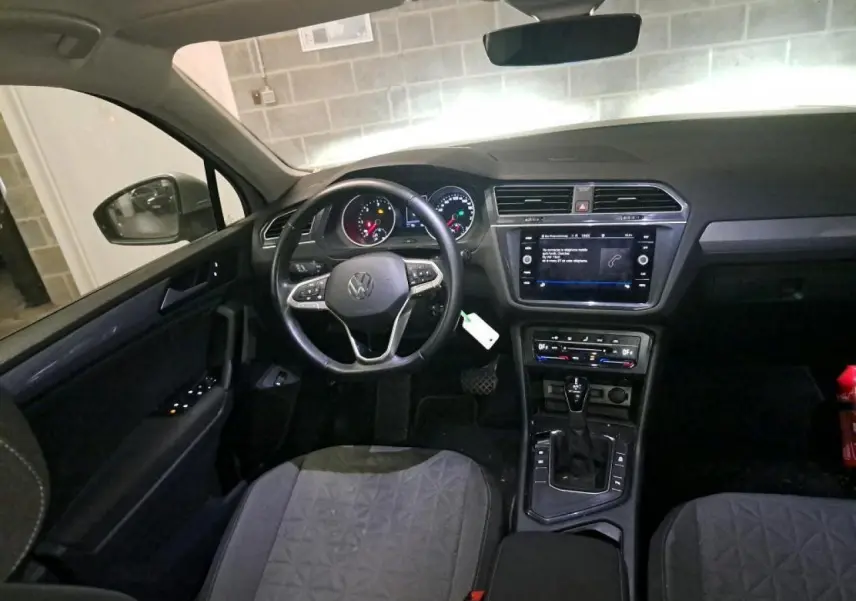 Vue intérieure du Volkswagen Tiguan 2022, tableau de bord et volant multifonctions en cuir, ambiance sombre et moderne.