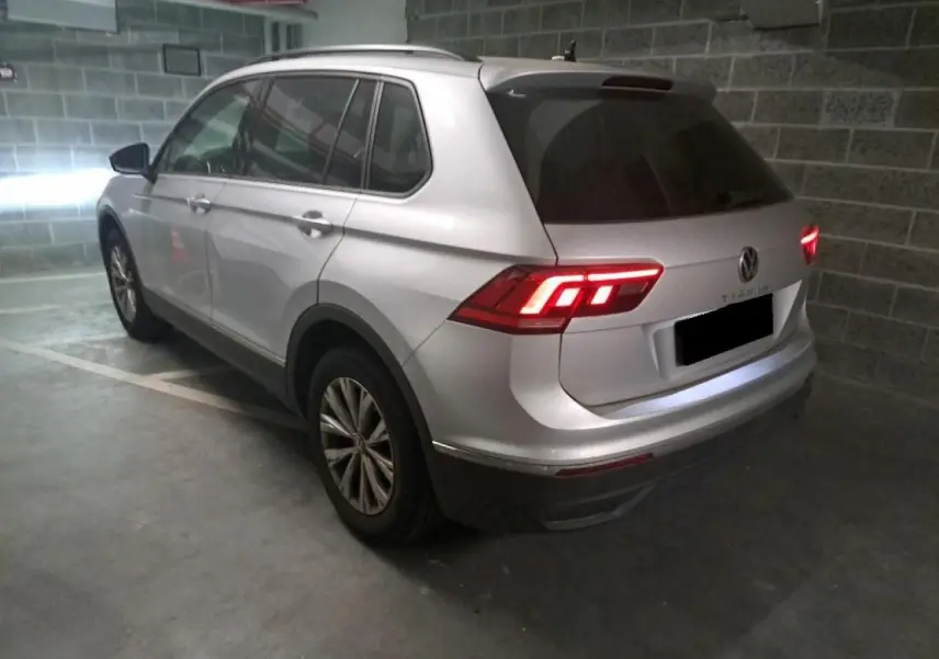 Volkswagen Tiguan argent Fleuret vu de l'arrière droit dans un parking, feux arrière LED allumés et vitres surteintées.