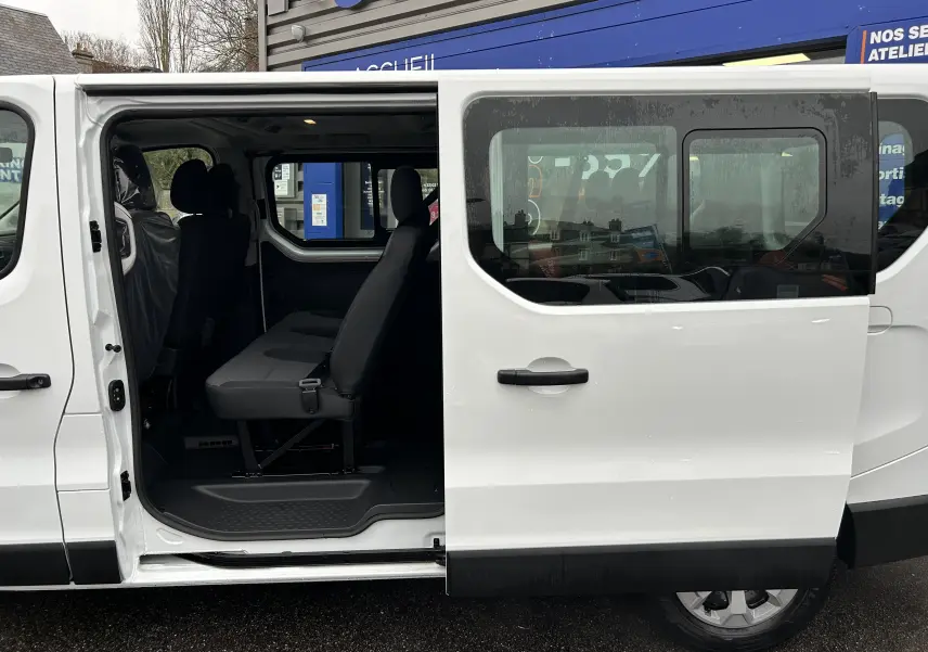 Vue latérale droite du Renault Trafic Combi blanc Glacier avec porte coulissante ouverte dévoilant la banquette arrière en tissu.