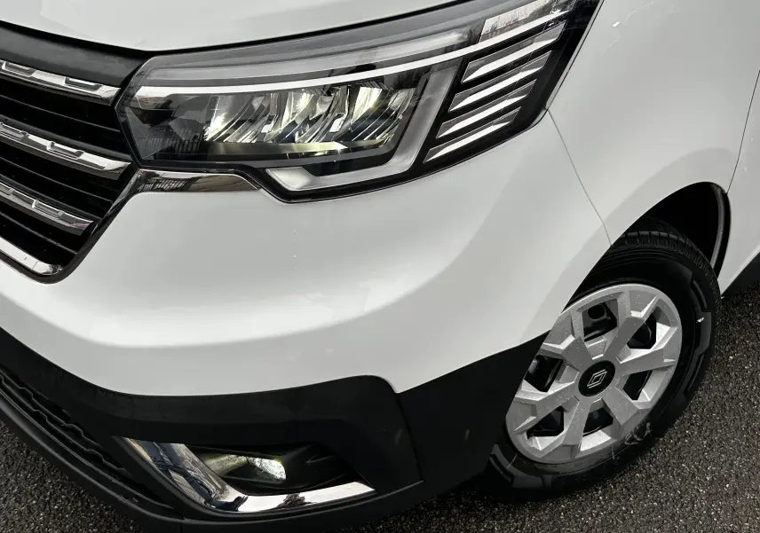 Gros plan sur l'avant droit blanc glacier du Renault Trafic Combi 2025, mettant en valeur le phare LED et la roue avec jante argentée.