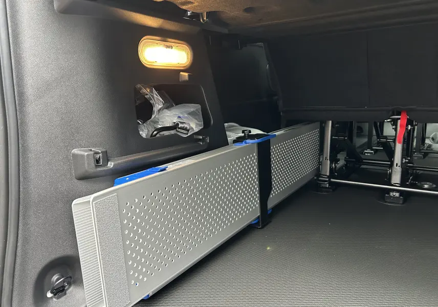 Vue intérieure arrière droite du Renault Trafic Combi blanc glacier, montrant le rangement sous banquette et l'éclairage intérieur.