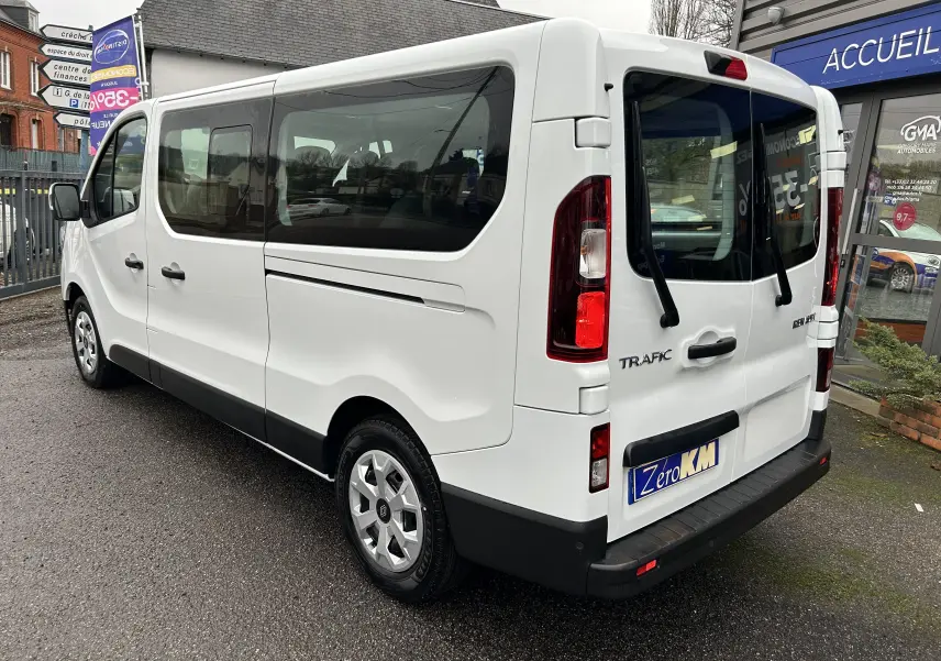 Vue 3/4 arrière droite du Renault Trafic Combi blanc glacier avec portes vitrées et hayon double ouvrant.
