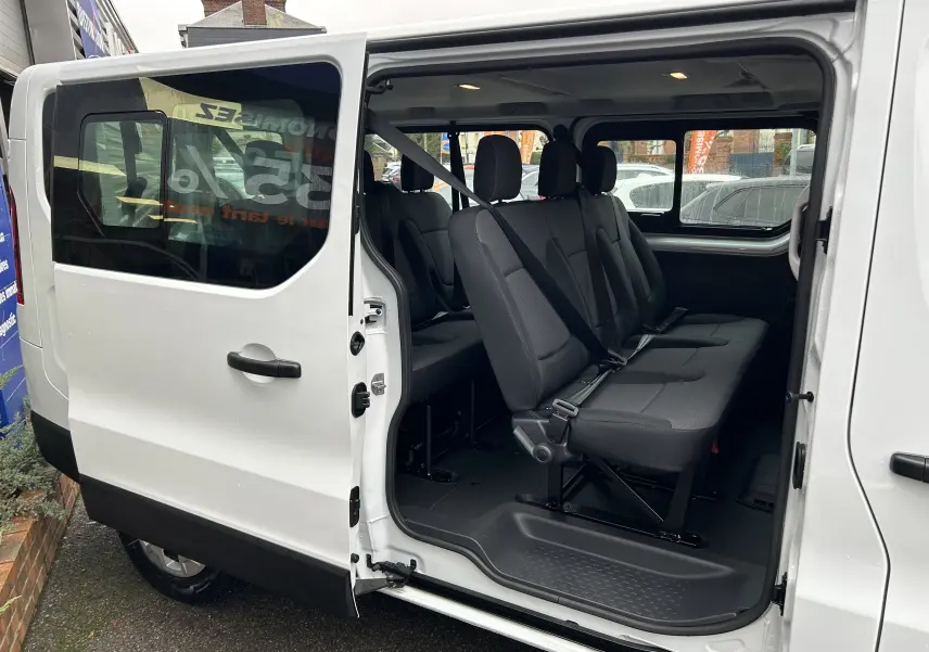 Vue latérale gauche du Renault Trafic Combi blanc Glacier avec porte coulissante ouverte dévoilant les sièges passagers en tissu noir.