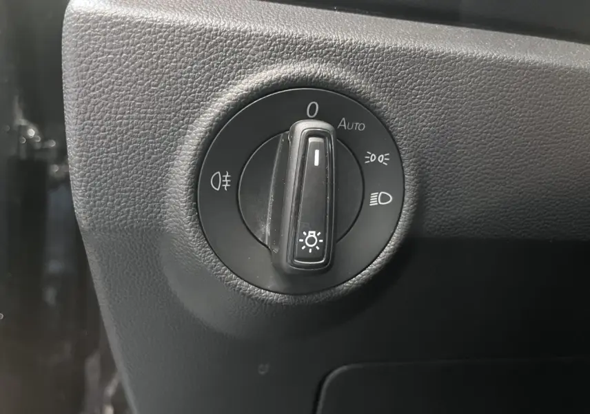 Gros plan sur le bouton de commande des phares dans l’habitacle noir du Volkswagen T-Roc Deep Black Pearlescent.