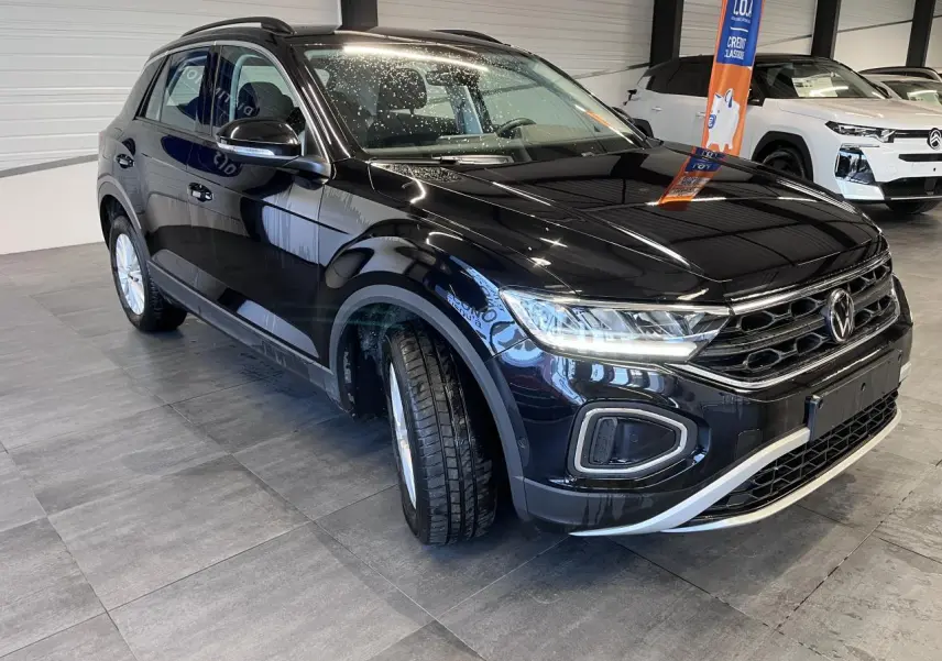 Volkswagen T-Roc Deep Black Pearlescent vue 3/4 avant droit en intérieur avec phares LED allumés.