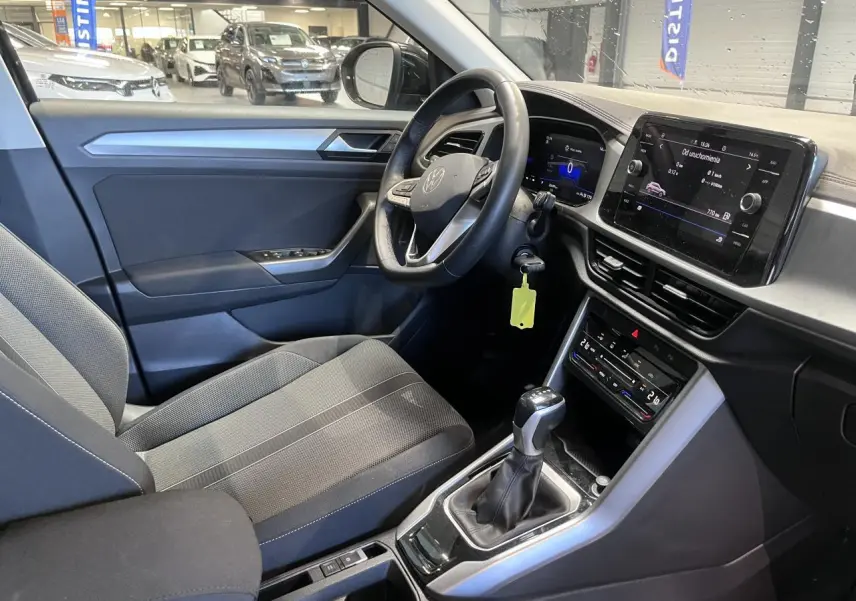 Intérieur avant droit du Volkswagen T-Roc 2025 avec sellerie tissu noire et tableau de bord digital.