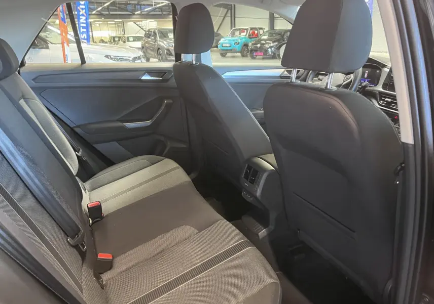 Vue intérieure arrière du Volkswagen T-Roc 2025 avec sellerie tissu noir et détails gris, montrant les sièges et aérateurs centraux.