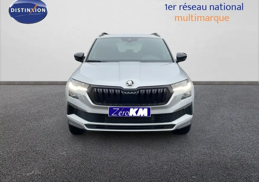 Vue avant d’un Skoda Karoq gris argent métallisé avec calandre noire et phares allumés sur fond neutre.