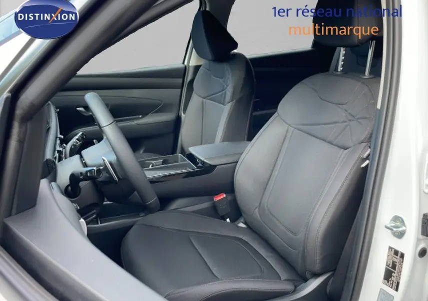 Vue intérieure côté conducteur du Hyundai Tucson blanc Atlas 2026, sièges tissu noir et tableau de bord moderne.