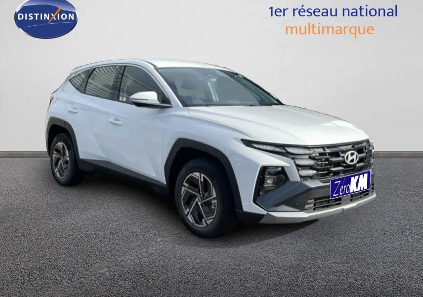 Hyundai Tucson blanc Atlas en 3/4 avant droit, SUV hybride avec calandre noire et jantes bi-ton.