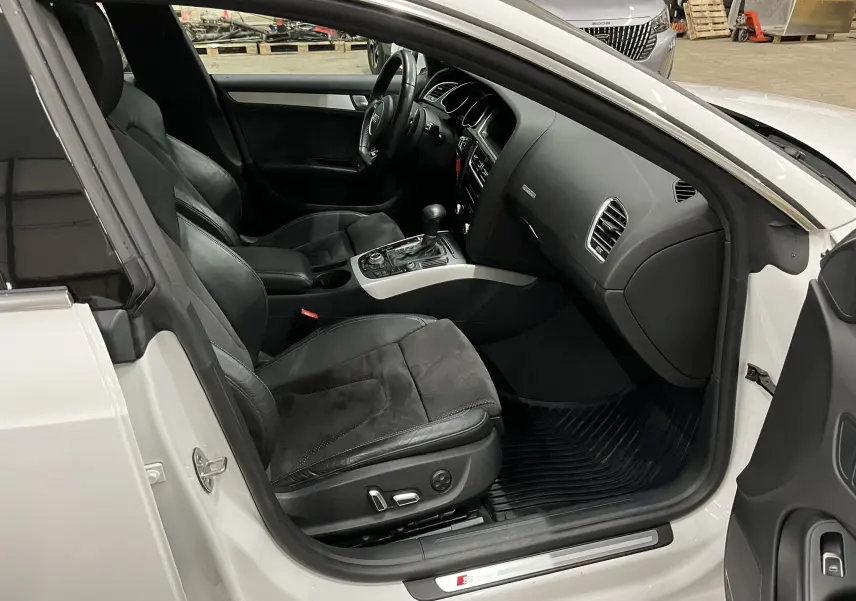 Intérieur côté conducteur d’Audi A5 Sportback blanc 2015, sièges noirs cuir/alcantara et console centrale avec boîte auto.
