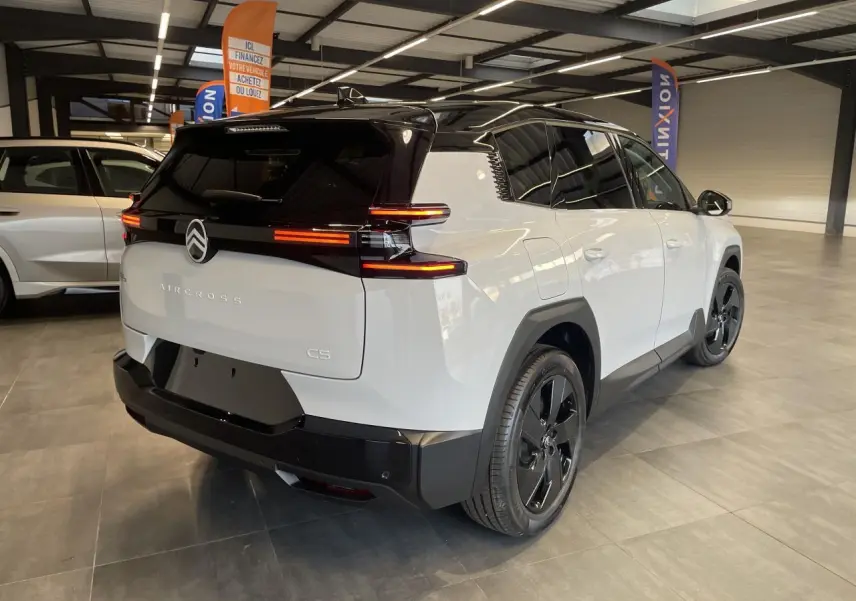 Vue 3/4 arrière droite du Citroën C5 Aircross blanc Okenite avec toit noir et feux arrière LED allumés en intérieur showroom.