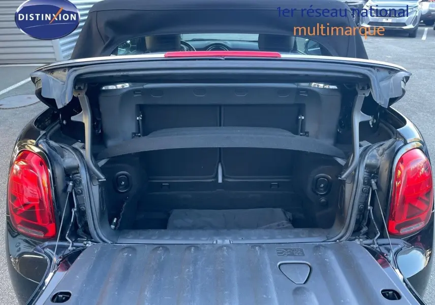 Coffre ouvert vu de l'arrière d'une MINI Cabriolet F57 noire, découvrant l'espace de rangement et la capote relevée.