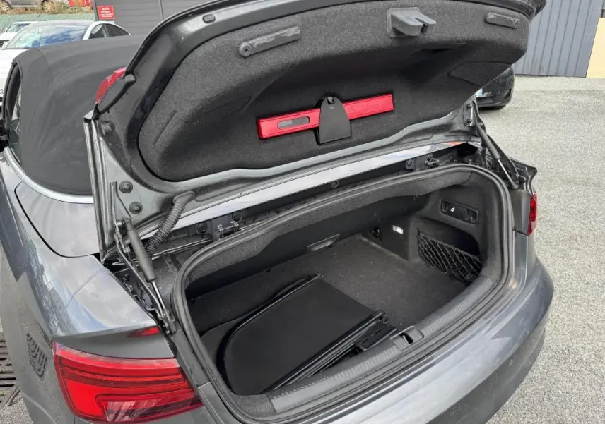 Coffre ouvert vu de l'arrière d'une Audi A3 Cabriolet gris avec capote noire et rangement intérieur visible.