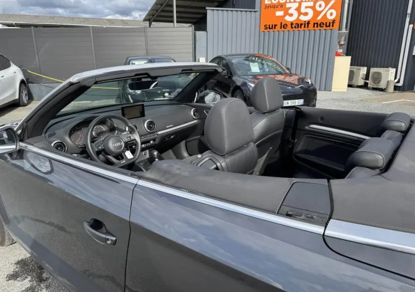 Vue côté gauche intérieur d'un cabriolet Audi A3 gris avec capote noire repliée et tableau de bord moderne.