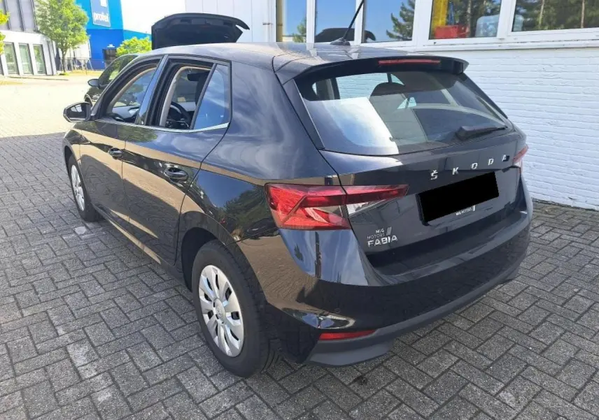 Vue 3/4 arrière droite d'une Skoda Fabia 2024 noire Magic avec hayon ouvert sur parking pavé.
