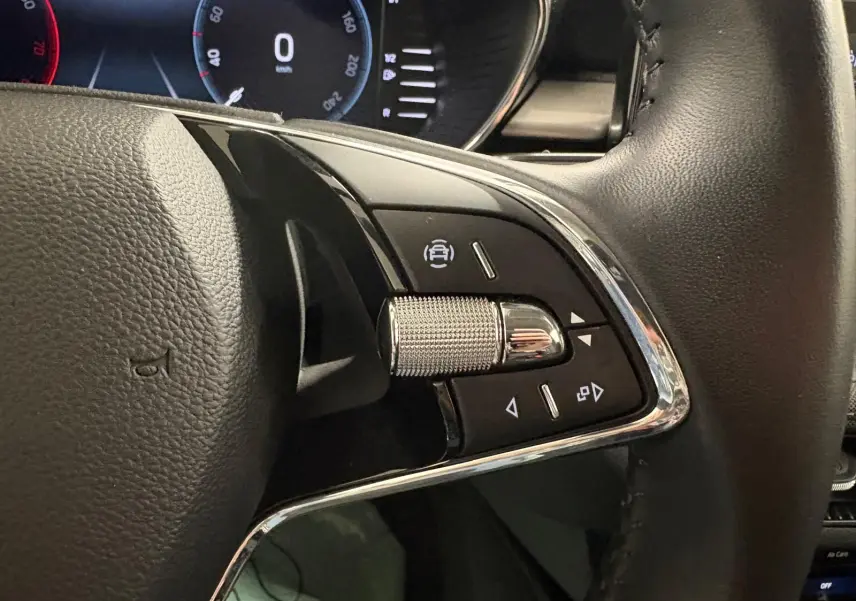 Gros plan sur les commandes gauche du volant en cuir noir de la Skoda Fabia 2023, avec molette métallique et boutons noirs.