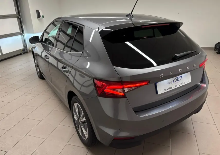 Vue 3/4 arrière droite d'une Skoda Fabia 2023 gris graphite métallisé avec vitres teintées et feux arrière allumés.