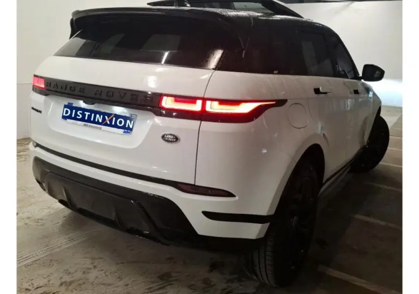 Vue 3/4 arrière droite d'un Range Rover Evoque blanc avec toit noir, feux arrière allumés et jantes noires.