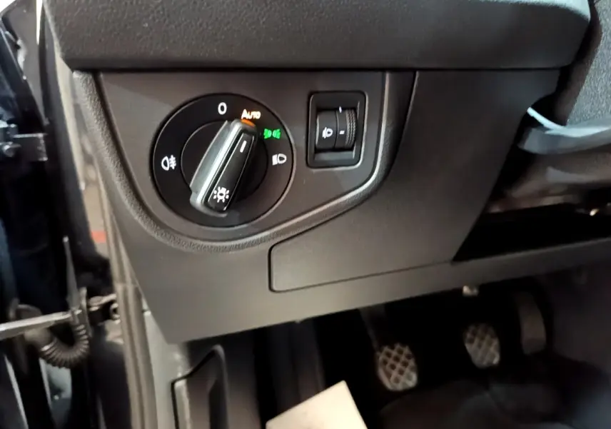 Gros plan sur le bouton de réglage des phares à gauche du tableau de bord d’un Volkswagen Taigo noir 2023.
