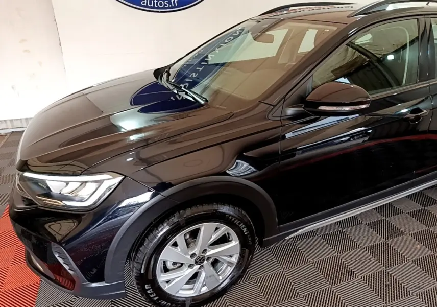 Volkswagen Taigo noir en 3/4 avant droit, avec phares LED et jantes alliage visibles en intérieur showroom.