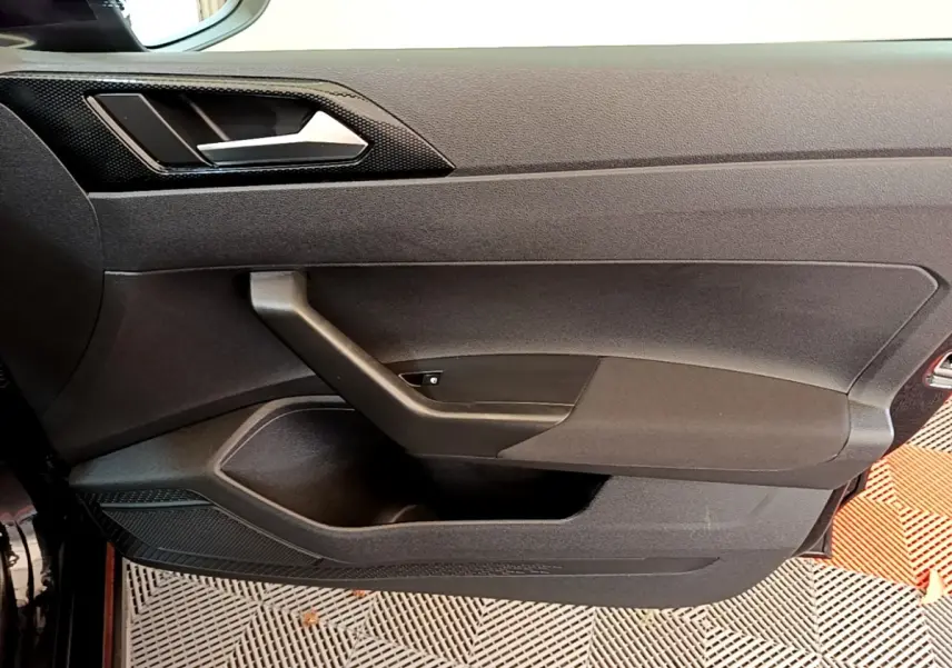 Vue rapprochée de la porte intérieure côté conducteur du Volkswagen Taigo noir, avec poignée et panneau de commande des vitres.