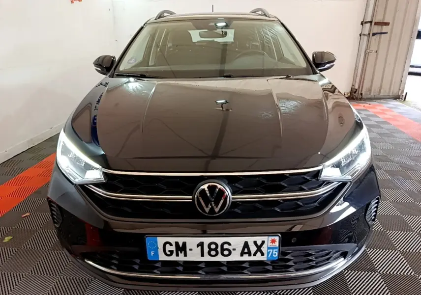 Vue avant d’un Volkswagen Taigo noir 2023 avec phares LED allumés dans un garage.