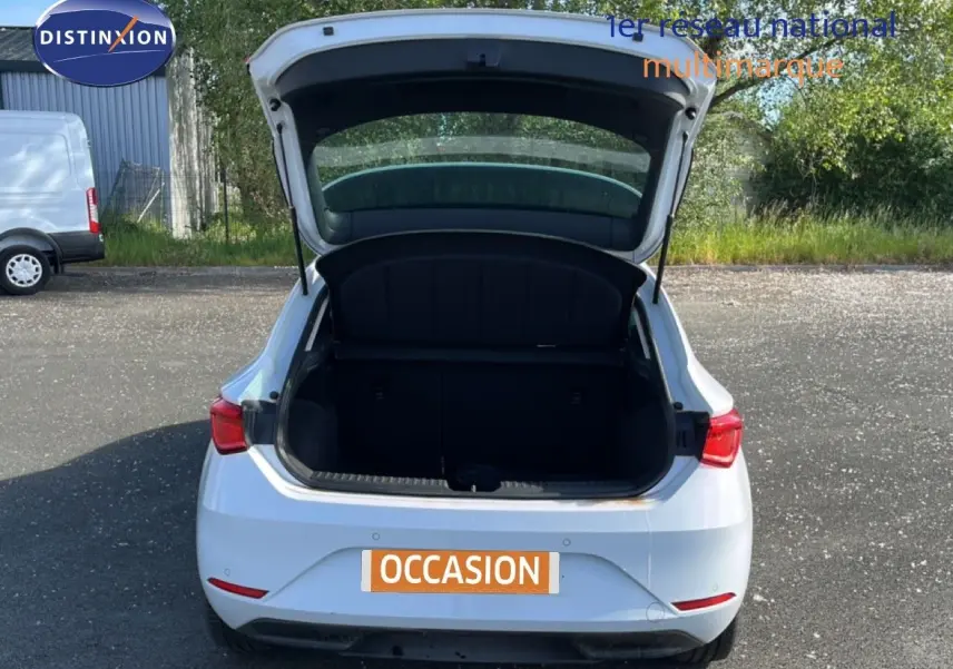 Vue arrière d'une SEAT Leon blanc neige 2025 avec coffre ouvert sur un parking extérieur.