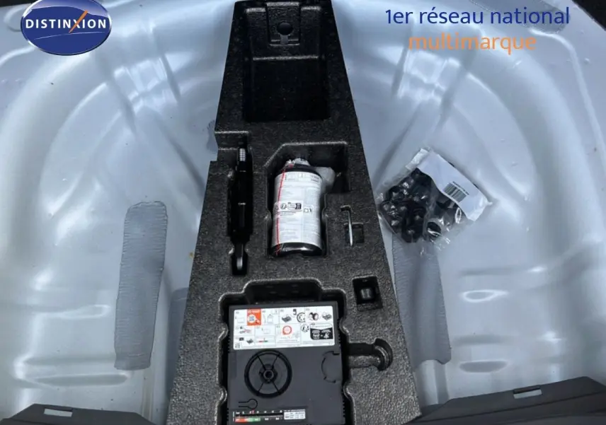 Vue plongeante sur le coffre ouvert d'une SEAT LEON blanc neige, montrant le rangement d'outils et kit de réparation.