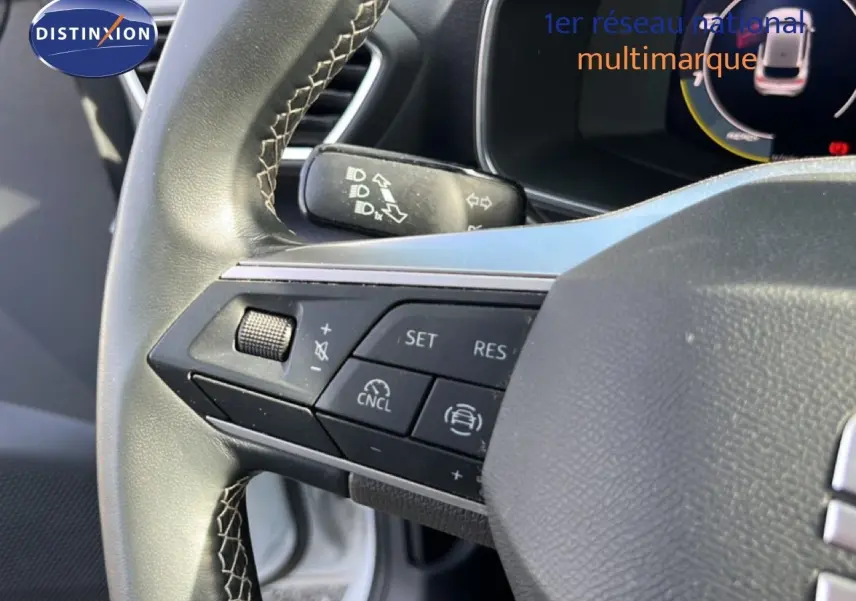 Gros plan sur le volant côté gauche de la SEAT LEON blanc neige, avec commandes intégrées visibles.