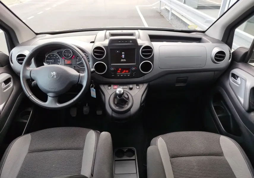 Vue intérieure avant du Peugeot Partner Tepee gris foncé, montrant le tableau de bord, volant, et console centrale avec boîte manuelle.