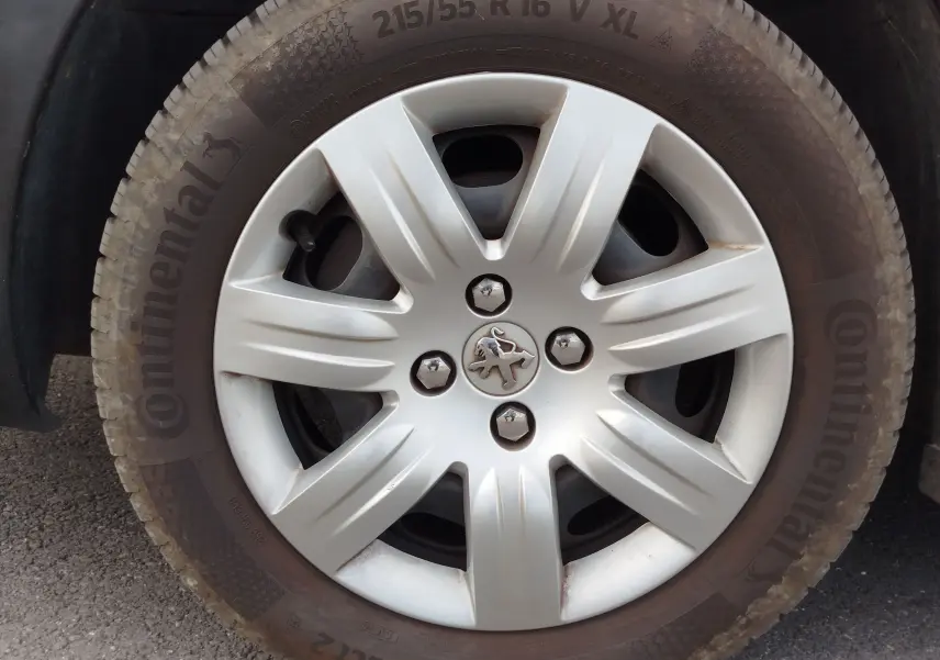 Gros plan sur la roue avant droite d’un Peugeot Partner Tepee gris foncé avec jante en alliage et logo lion au centre.