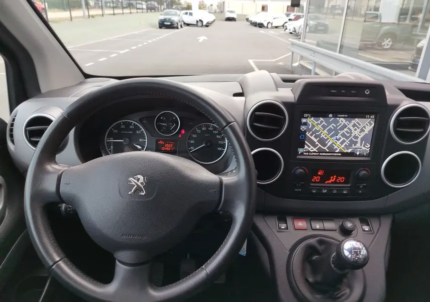 Vue intérieure du tableau de bord du Peugeot Partner Tepee gris foncé, avec volant, écran GPS et levier de vitesses manuel.