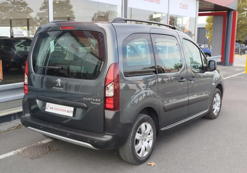 Vue 3/4 arrière droite d’un Peugeot Partner Tepee gris foncé stationné, avec vitres teintées et barres de toit.