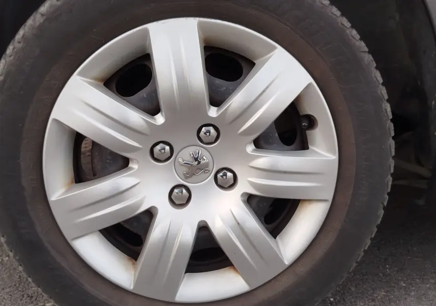 Gros plan sur la roue avant droite du Peugeot Partner Tepee gris foncé, avec enjoliveur argenté et logo lion central.
