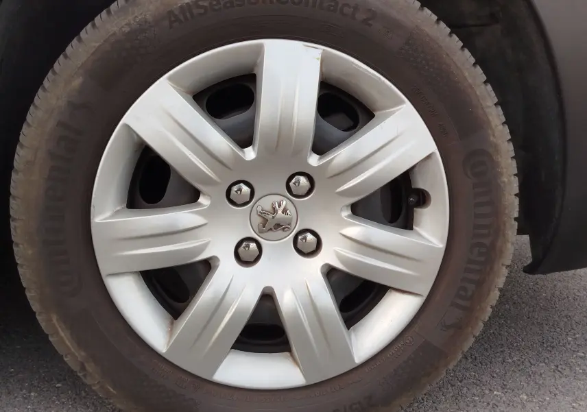 Gros plan sur la roue avant gauche d’un Peugeot Partner Tepee gris foncé, avec jante en alliage et logo lion au centre.