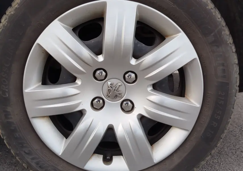 Gros plan sur la jante argentée avec logo Peugeot au centre, montée sur pneu Michelin d’un Partner Tepee gris foncé.