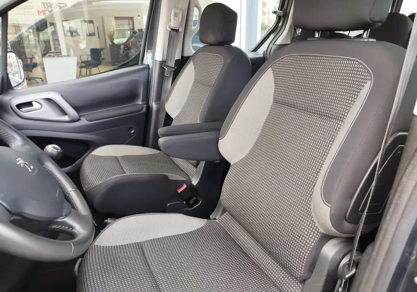 Vue intérieure côté conducteur du Peugeot Partner Tepee gris foncé, mettant en valeur les sièges tissu gris à motifs et l'accoudoir central.