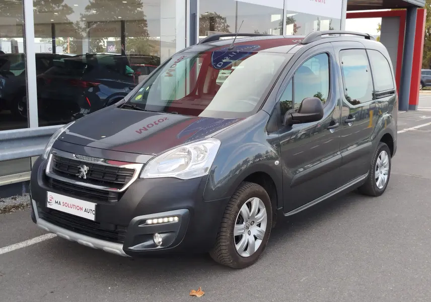 Peugeot Partner Tepee gris foncé en 3/4 avant droit, avec barres de toit et feux LED diurnes visibles.